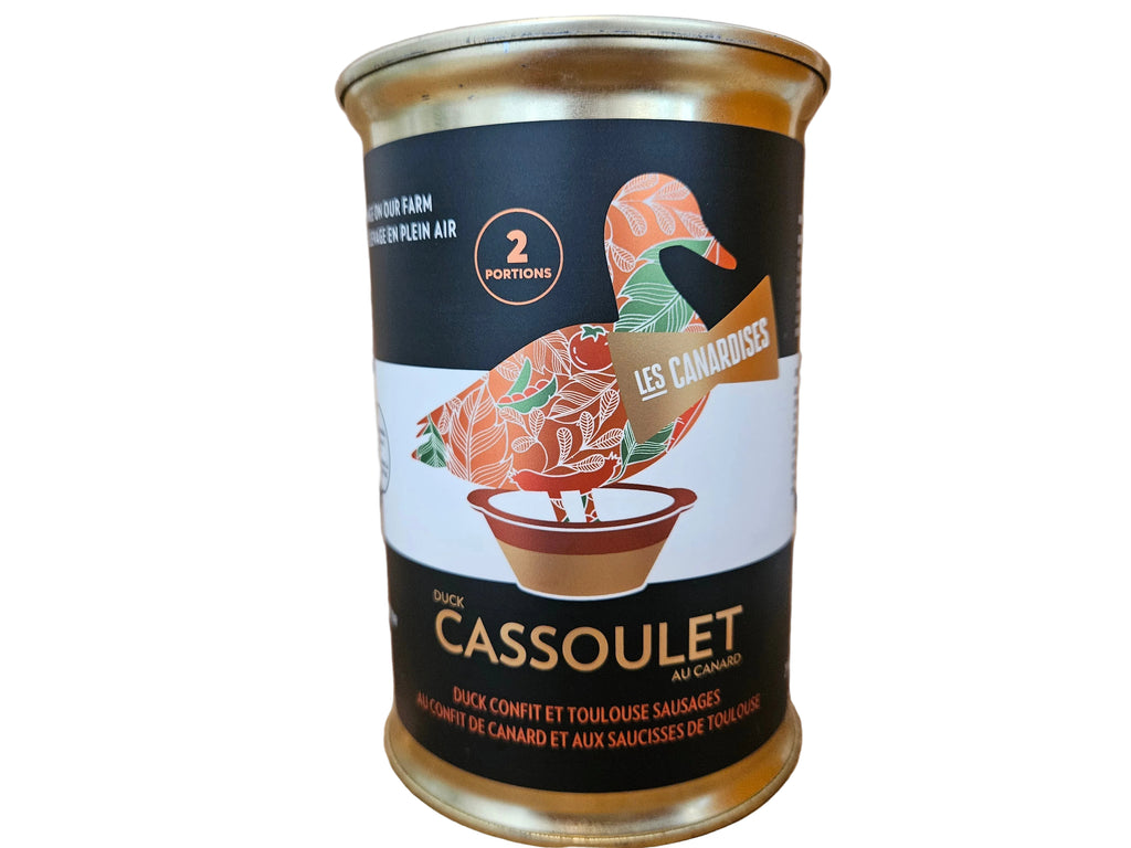 A can of Duck Cassoulet from Les Canarisses, featuring a black and white label with a colorful patterned duck illustration, set on a rustic wooden cutting board.